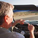 A couple driving a classic convertible along a country road.