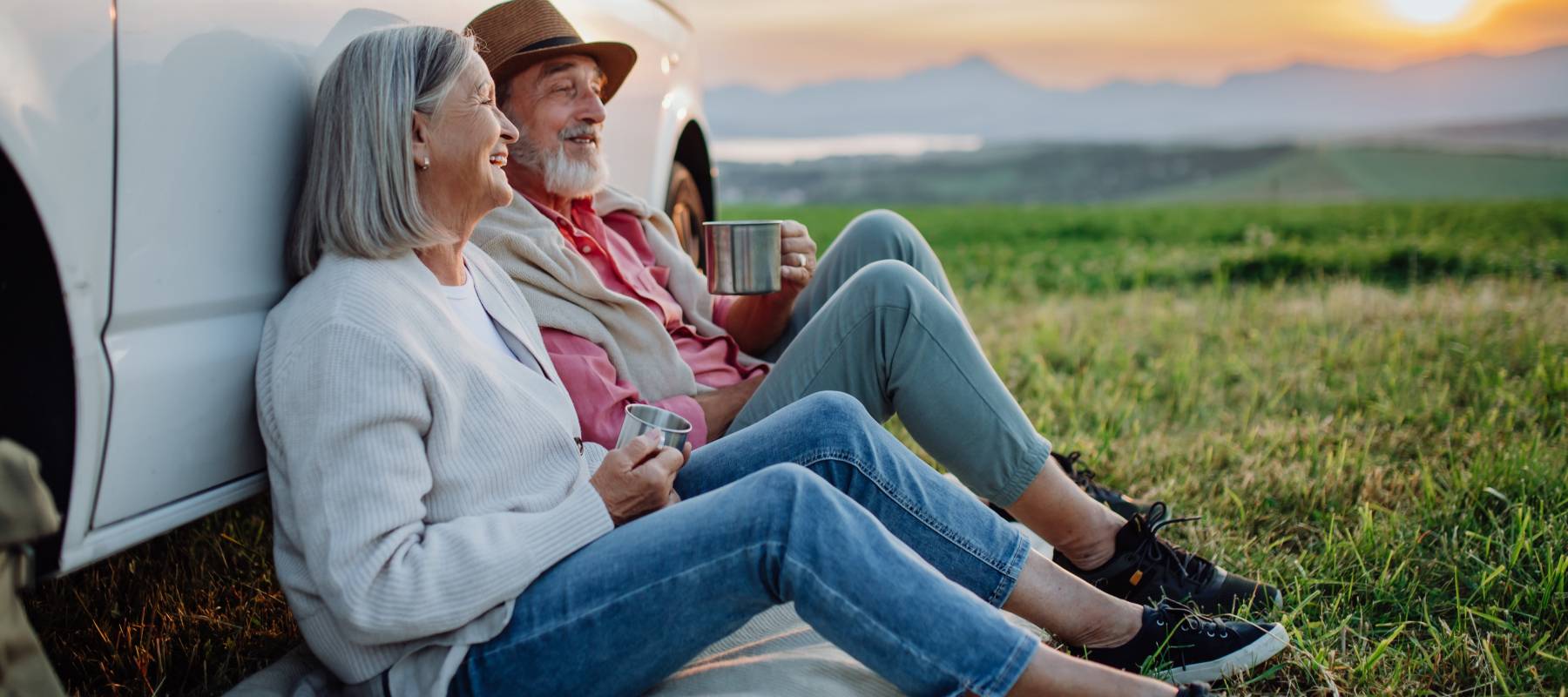 senior Caucasian couple sitting by car and drinking coffee after long drive during their roadtrip
