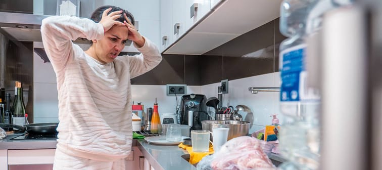 Overwhelmed woman stands in a messy kitchen