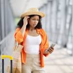 A young Black woman in an airport, looking at her phone with concern
