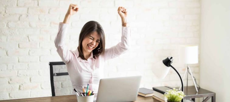 Excited woman using the computer and celebrating some good news with her arms up
